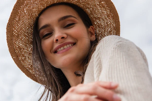 Низький кут зору щасливої молодої жінки в солом'яному капелюсі дивиться на камеру — стокове фото