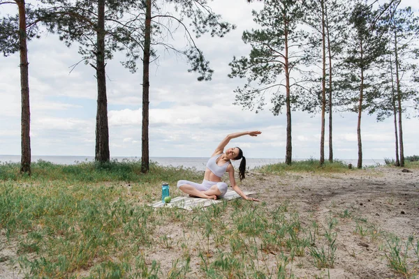 Brunette jeune femme en vêtements de sport assis dans la pose de lotus et étirement sur tapis de yoga — Photo de stock