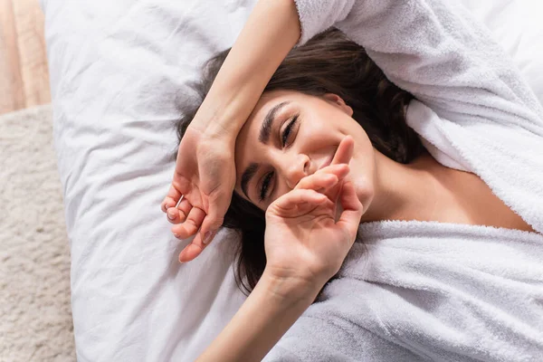 Blick von oben auf zufriedene Frau, die auf dem Bett liegend in die Kamera blickt — Stockfoto