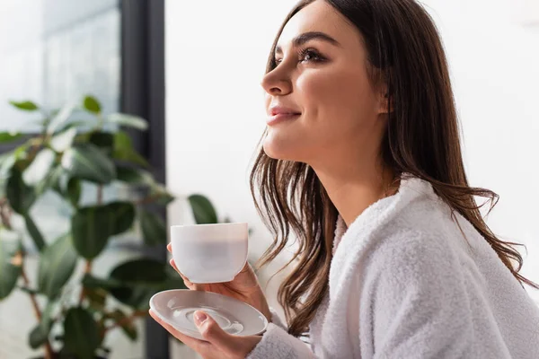 Happy young woman holding cup of coffee and saucer — Stock Photo