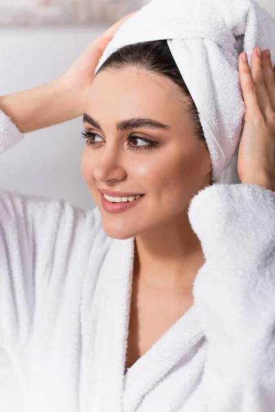 Mujer sonriente ajustando la toalla en la cabeza en casa - foto de stock