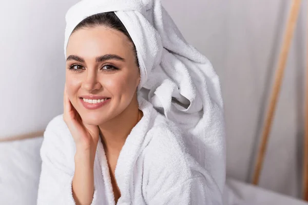 Mujer alegre en toalla en la cabeza y albornoz sonriendo en el dormitorio — Stock Photo