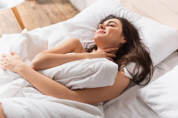 High angle view of young pleased woman resting under white blanket on bed — Stock Photo