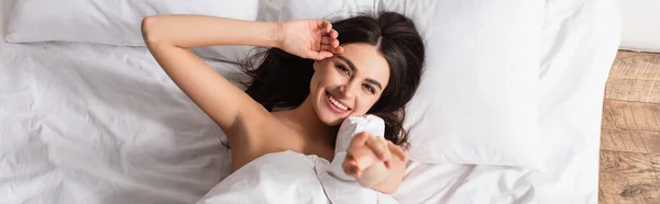 Vista superior de la joven mujer complacida acostada debajo de la manta y el gesto en el dormitorio, pancarta - foto de stock