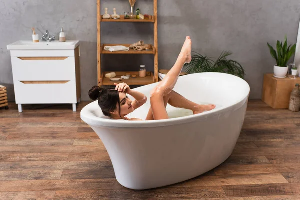 Jeune femme joyeuse avec jambe levée prenant bain dans la baignoire moderne — Photo de stock