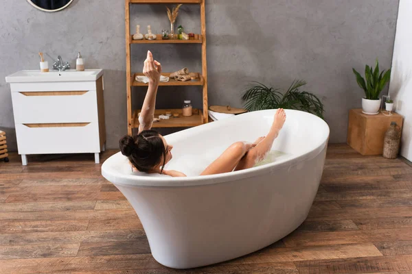 Junge fröhliche Frau mit erhobener Hand badet in moderner Badewanne — Stockfoto