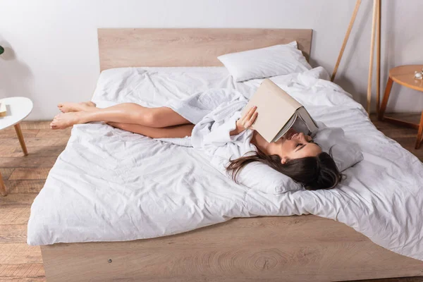 Mujer feliz en albornoz acostada en la cama y leyendo libro - foto de stock