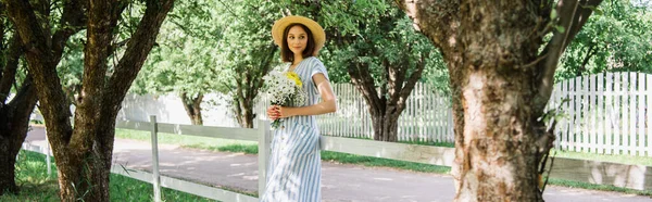 Красива жінка в солом'яному капелюсі тримає квіти в парку, банер — стокове фото