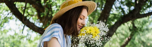 Vue latérale de la femme au chapeau de soleil sentant les fleurs à l'extérieur, bannière — Photo de stock