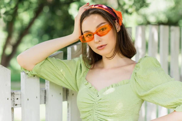 Mulher bonita em lenço de cabeça e óculos de sol em pé perto da cerca — Fotografia de Stock