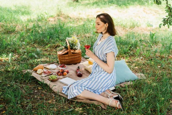 Vista lateral da mulher no vestido de verão segurando vinho no cobertor no parque — Fotografia de Stock