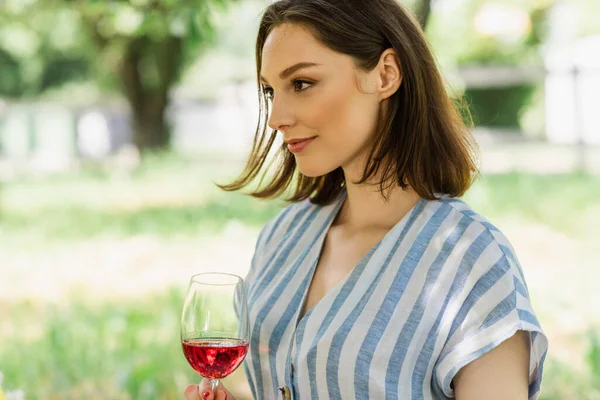 Mujer joven sosteniendo copa de vino en el parque - foto de stock