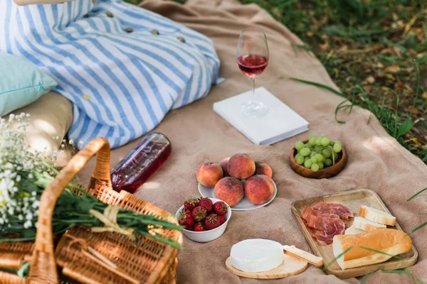 Cropped view of tasty food and wine near basket and woman on blanket in park — Stock Photo