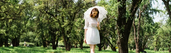 Улыбающаяся женщина в платье держит зонтик в парке, баннер — стоковое фото