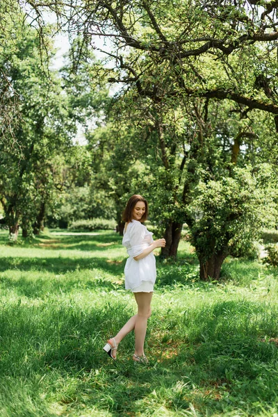 Glückliche junge Frau im Sommerkleid steht im Park — Stockfoto