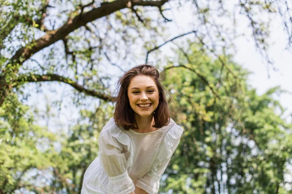 Jolie femme en robe blanche souriant à la caméra dans le parc d'été — Photo de stock