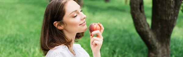 Pretty woman closing eyes while holding fresh peach in park, banner — Stock Photo