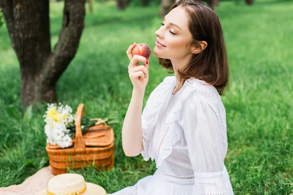 Женщина с закрытыми глазами держит персик в летнем парке — стоковое фото