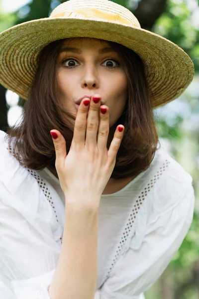 Erstaunte Frau mit Sonnenhut bedeckt Mund im Freien — Stockfoto