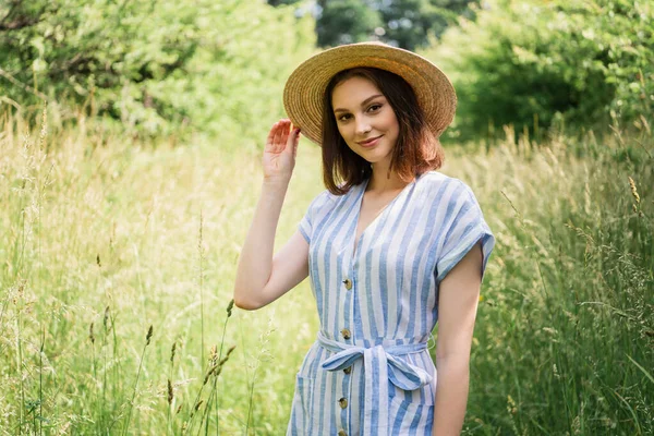 Mujer en vestido a rayas sosteniendo sombrero de paja en el parque - foto de stock