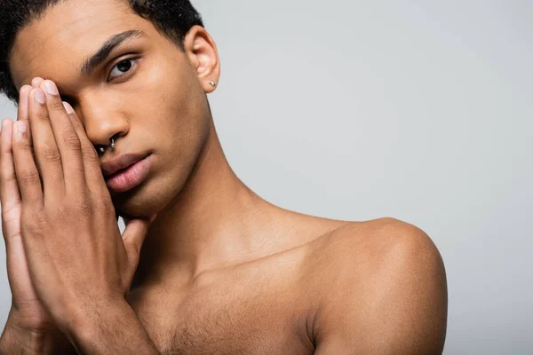 Sin camisa afroamericano chico con piercing cogido de la mano cerca de la cara aislado en gris, concepto de belleza - foto de stock