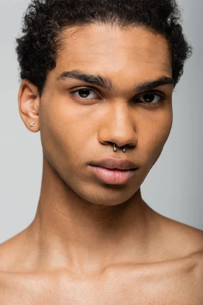 Retrato del joven afroamericano con piercing mirando a la cámara aislada en gris, concepto de belleza - foto de stock