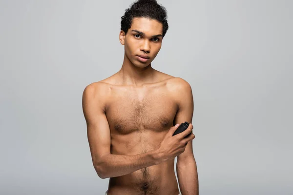 Shirtless, young african american man looking at camera while spraying antiperspirant isolated on grey — Stock Photo