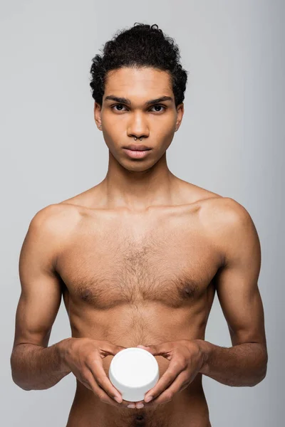 Vorderseite der hemdlosen afrikanisch-amerikanischen Mann hält kosmetische Creme isoliert auf grau — Stockfoto