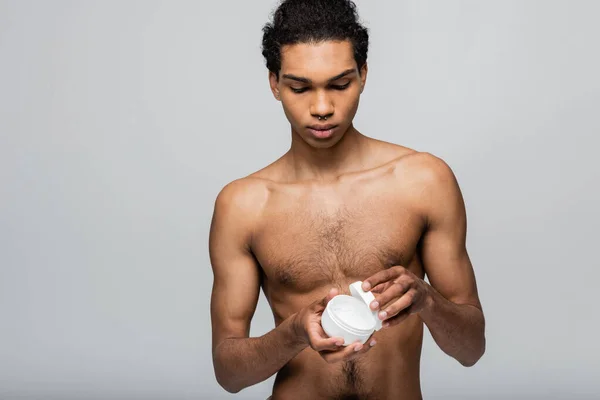 Sin camisa afroamericano chico apertura contenedor con crema cosmética aislado en gris - foto de stock