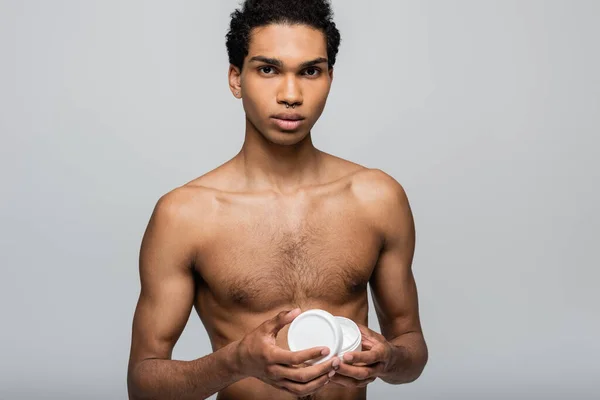 Shirtless african american guy opening cosmetic cream while looking at camera isolated on grey — Stock Photo