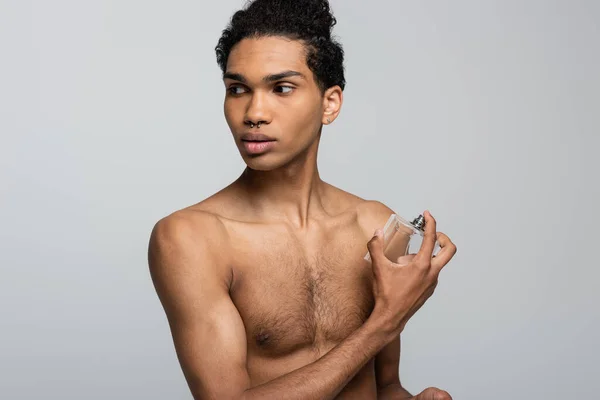 Без сорочки афроамериканський хлопець наносить парфуми, дивлячись ізольовано на сірий — стокове фото