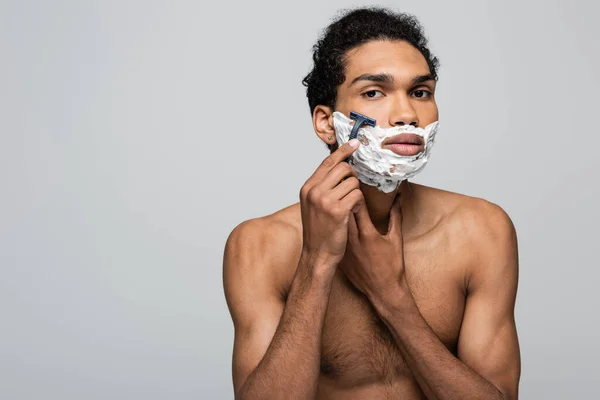 Без сорочки афроамериканський чоловік використовує запобіжну бритву під час гоління ізольовано на сірому — стокове фото