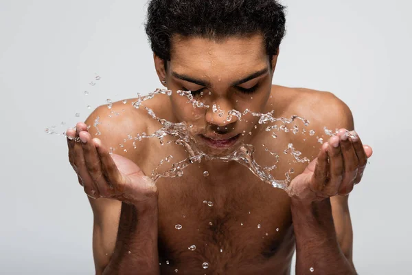 Homem afro-americano sem camisa lavando rosto com água doce isolada em cinza — Fotografia de Stock