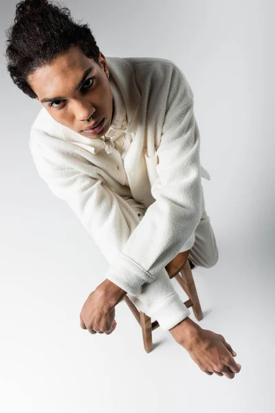 Overhead view of trendy african american guy in white clothes looking at camera on grey background — Stock Photo