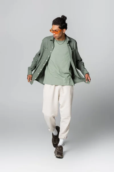 Young african american man in trendy clothes and sneakers walking on grey background — Stock Photo