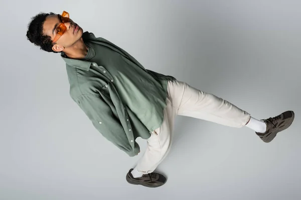 Vista aérea del hombre afroamericano de moda en gafas con estilo mirando a la cámara sobre fondo gris - foto de stock