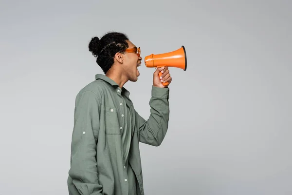 Side view of stylish african american man screaming in megaphone isolated on grey — Stock Photo
