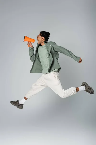 Elegante afro americano cara gritando em megafone enquanto levita no fundo cinza — Fotografia de Stock