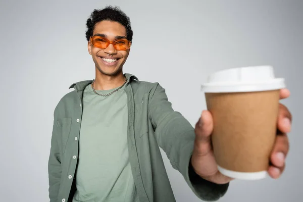 Cheerful and stylish african american guy holding blurred paper cup isolated on grey — Stock Photo