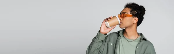 Young african american man in stylish shirt and eyeglasses drinking coffee isolated on grey, banner — Stock Photo