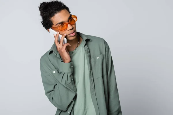 Афроамериканський хлопець у сорочці та окулярах говорить на смартфоні ізольовано на сірому — стокове фото