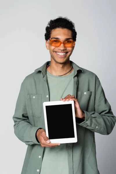 Joyeux homme afro-américain souriant à la caméra tout en montrant tablette numérique isolé sur gris — Photo de stock