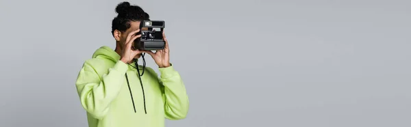 African american man in hoodie taking picture on vintage camera isolated on grey, banner — Stock Photo