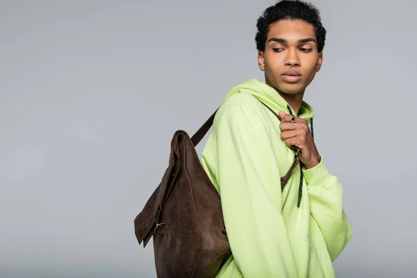 Стильный африканский американец в зеленой толстовке, с кожаным рюкзаком, изолированным на сером — стоковое фото