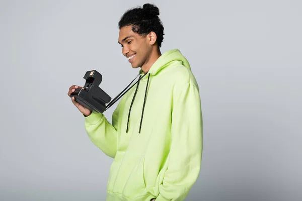 Cheerful african american man in stylish hoodie taking picture on vintage camera isolated on grey — Stock Photo