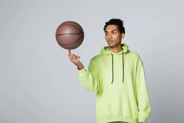 African american guy in stylish hoodie playing with basketball isolated on grey — Stock Photo