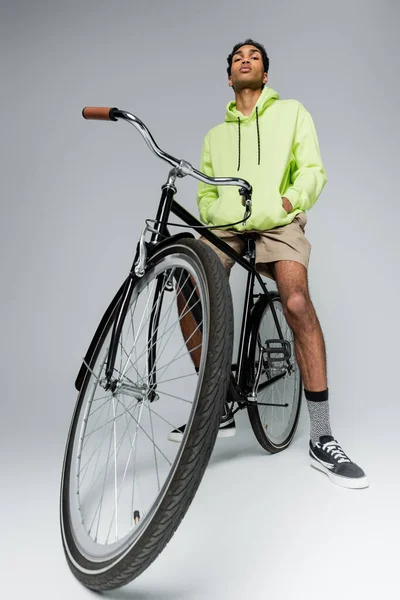 Confiante e elegante cara americano africano com bicicleta olhando para a câmera no fundo cinza — Fotografia de Stock