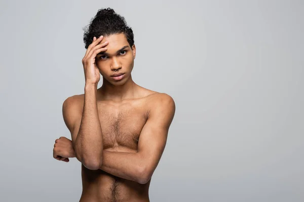 Sem camisa afro-americano homem de mãos dadas perto do rosto enquanto olha para a câmera isolada em cinza, conceito de beleza — Fotografia de Stock