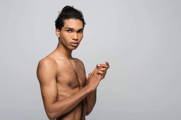 Молодой, без рубашки африканский американец позирует изолированно на сером и смотрит в камеру, концепция красоты — стоковое фото