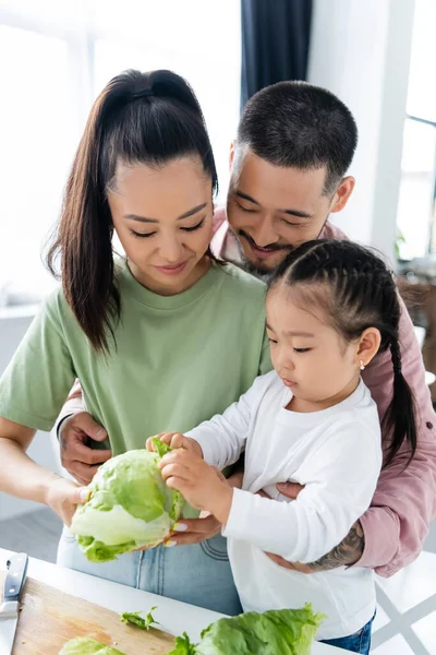 Happy asian family looking at fresh lettuce in kitchen — Stock Photo